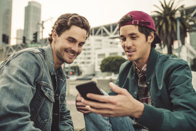 Two smiling young men sharing cell phone outdoors