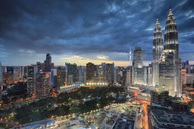 Illuminated buildings in city against cloudy sky