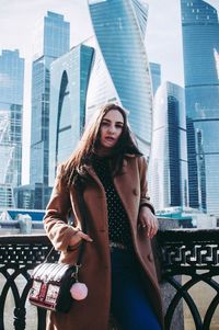 Portrait of smiling young woman against modern city