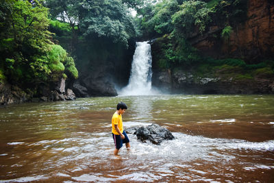 Full length of boy standing against waterfall