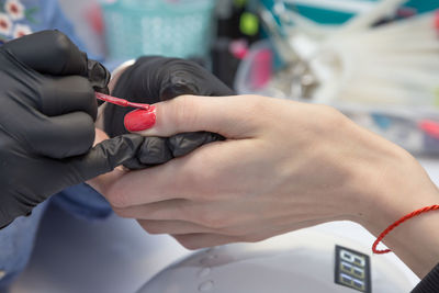 Cropped hands of manicurist applying nail polish on finger of woman