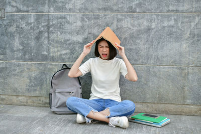 Frustrated young woman shouting while sitting book against gray wall
