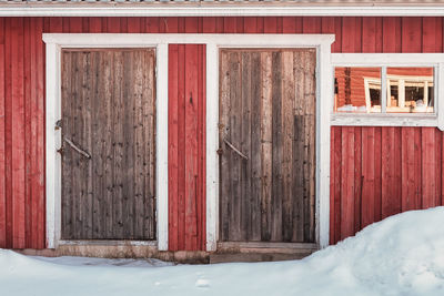 An old wooden building has two doors and a window beautifully framed with white painted wood.