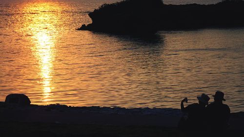 Silhouette people photographing sea against sky during sunset