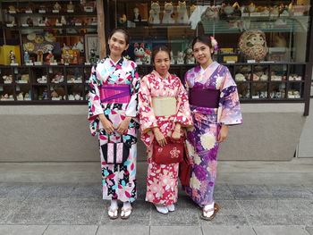 Portrait of smiling females in kimono standing against store