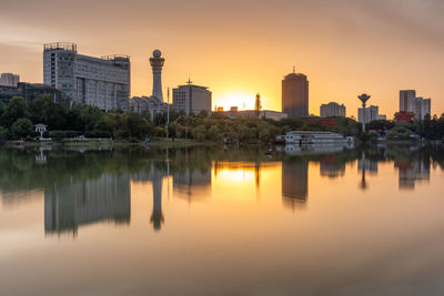 Reflection of buildings in lake against sky during sunset