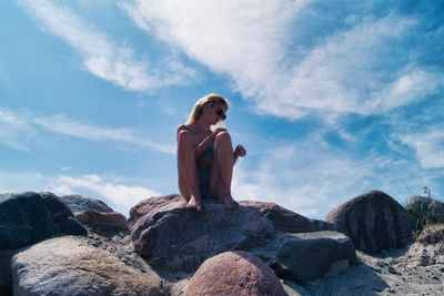 Low angle view of woman in bikini sitting on rock at beach against sky, timmendorfer strand 