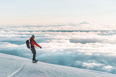 Snowboarder riding down mountain at sunset above clouds