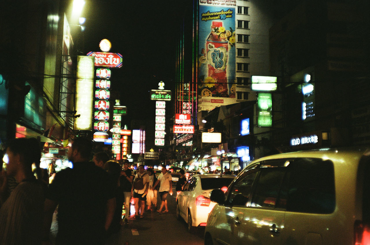 PEOPLE ON ILLUMINATED STREET AMIDST BUILDINGS IN CITY