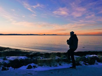 Man standing on beach against sky during sunset