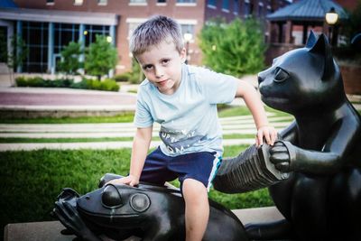 Portrait of boy sitting on statues in garden against building