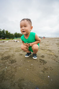Boy crouching at beach against sky