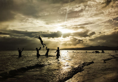 Silhouette people enjoying at beach against sky during sunset