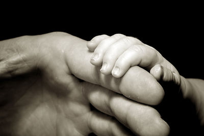 Cropped image of parent holding baby hand against black background