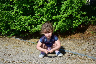 Full length of girl crouching on footpath against plants