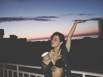 Young woman drinking water from railing against sky