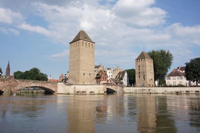 Arch bridge over river by buildings against sky