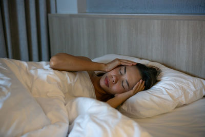 Woman with head in hand lying on bed at home