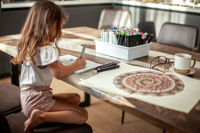 Rear view of girl holding food on table