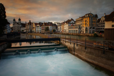 Bridge over river by buildings in city against sky