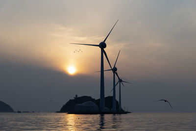 Silhouette of wind turbines in sea against sunset sky