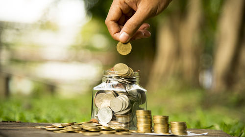 Cropped hand of man putting coin in jar on table