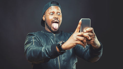 Close-up portrait of man using phone against black background