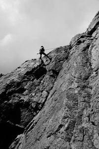 Low angle view of man mountain climbing against sky