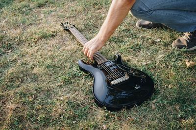 Low section of man picking up electric guitar on grassy field