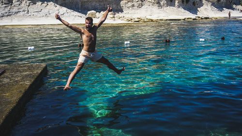 Full length of shirtless man jumping in sea