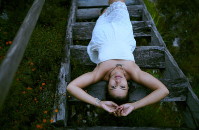 High angle portrait of young woman relaxing on wooden ladder