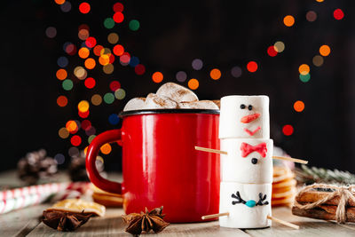 Red enamel mug of hot chocolate with marshmallow snowman on christmas background