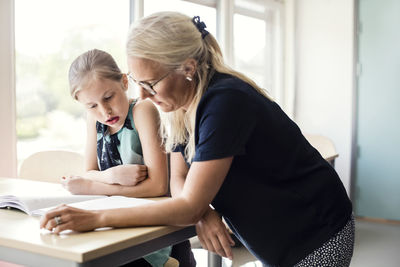 Teacher helping student with book in classroom