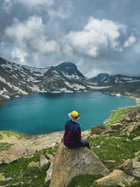 Rear view of woman sitting on rock against sky