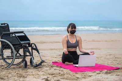 Woman sitting on beach by sea against sky