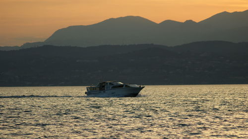 Boat sailing on sea against mountains during sunset