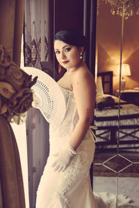 Portrait of woman in dress holding hand fan at home