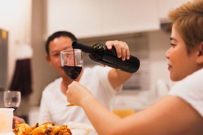 Husband pouring red wine into his wife glass during dinner at home.