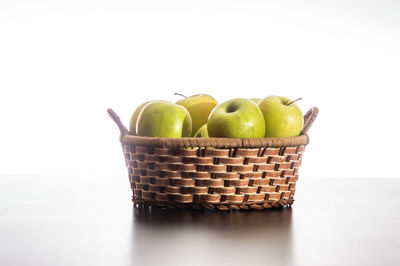 Fruits in basket on table against white background