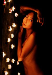 Side view portrait of topless woman lying down by illuminated candles at night