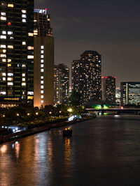 Illuminated buildings by river against sky in city at night