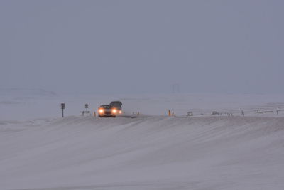 Snow covered land by road against sky during winter