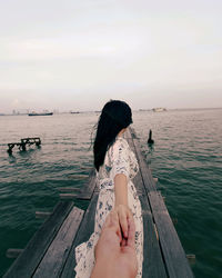 Low section of woman sitting on pier over sea against sky