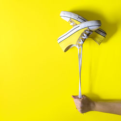 Cropped hand of woman holding shoes against yellow background