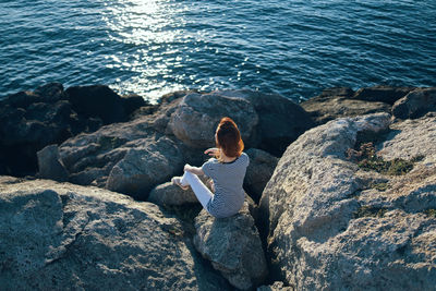 Rear view of woman sitting on rock by sea