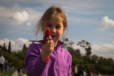 Portrait of cute smiling girl holding strawberry and scissors at farm