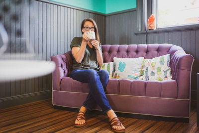 Full length portrait of young woman sitting on sofa