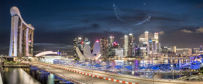 Illuminated city by river against sky at night