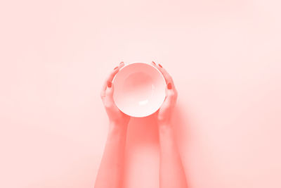 Close-up of hand holding pink balloons against white background