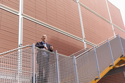 Businessman leaning on staircase railing near building